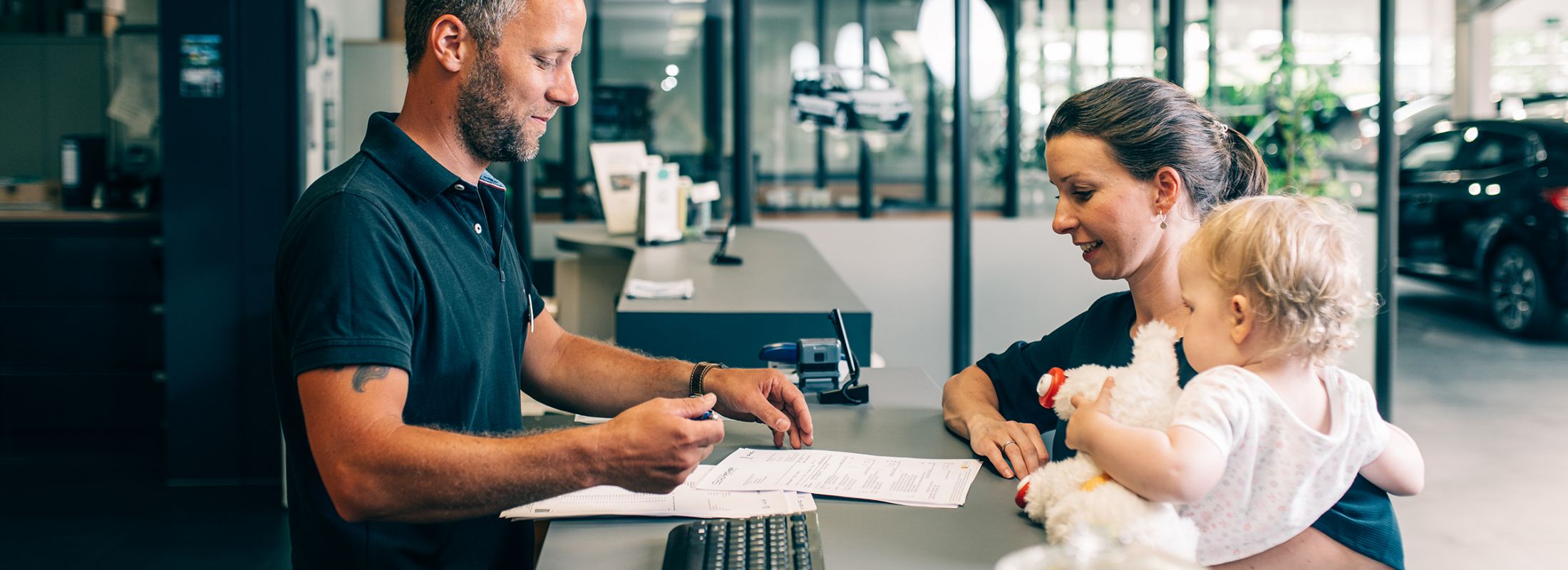 Unser Mitarbeiter berät eine Kundin mit Kind im Arm an unserer Empfangstheke