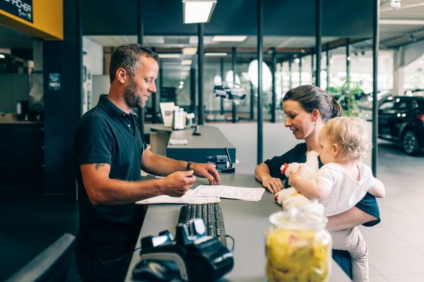Unser Mitarbeiter berät eine Kundin mit Kind im Arm an unserer Empfangstheke