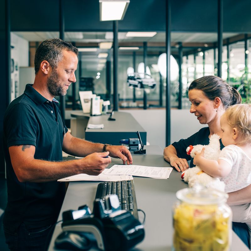 Unser Mitarbeiter berät eine Kundin mit Kind im Arm an unserer Empfangstheke