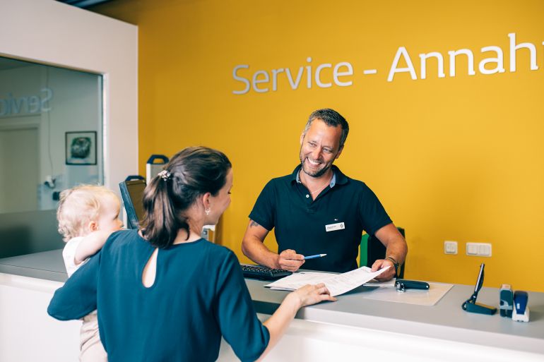 Mitarbeiter berät eine Kundin mit Kind am Serviceschalter