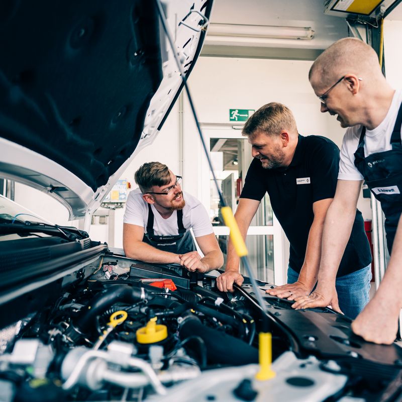 Drei Mitarbeiter schauen gemeinsam in den Motorraum eines Fahrzeugs